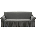 4-seater grey stretch sofa cover with ruffled skirt on a living room couch