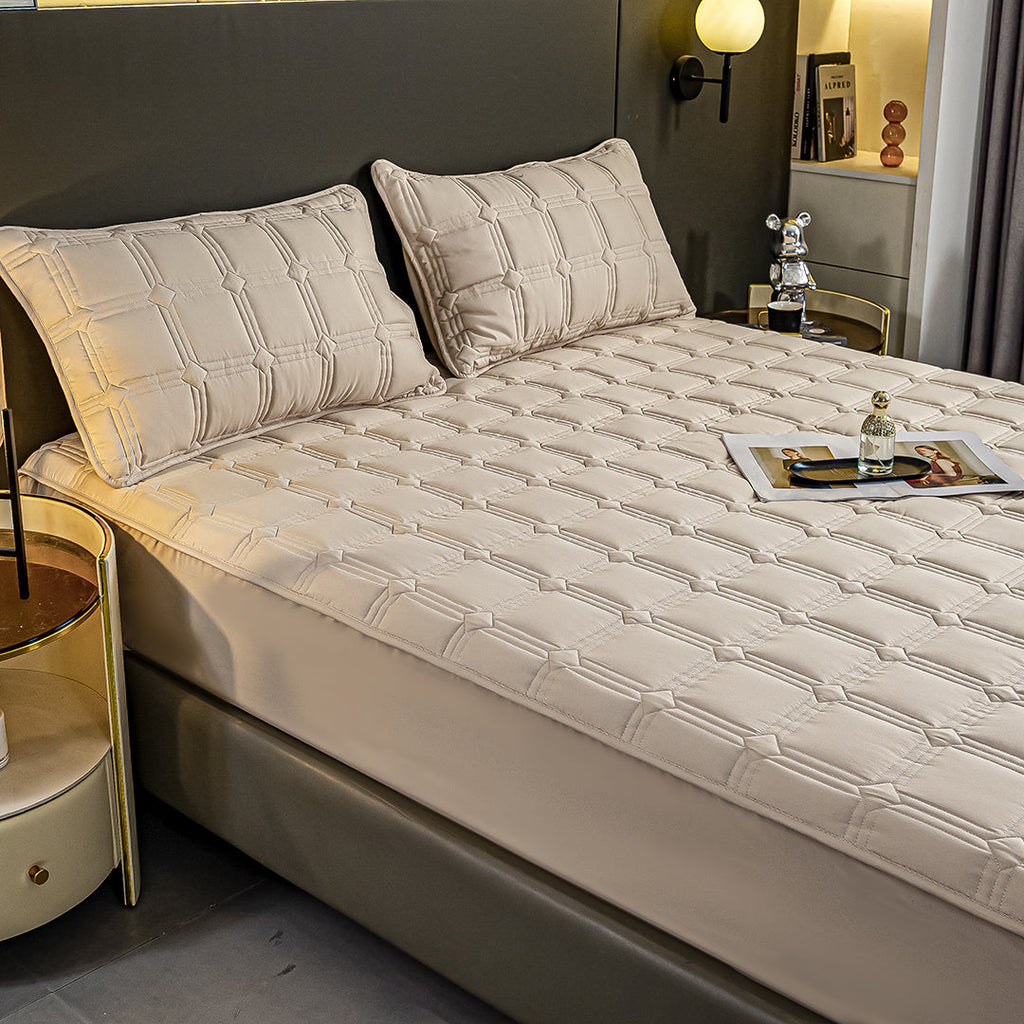 Beige quilted stretchable mattress cover and two matching pillow cases displayed on a bed. — view 3