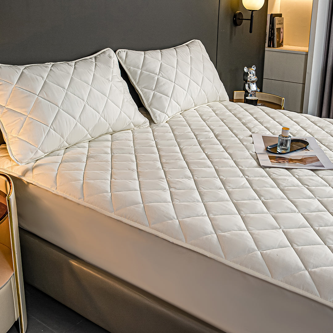 White quilted mattress cover and two matching pillow protectors displayed on a well-made comfortable bed — view 3