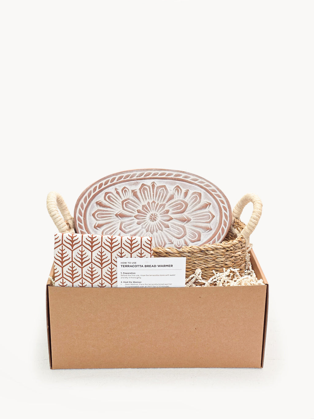 Terracotta bread warmer with engraved flower, woven seagrass serving basket, and natural cotton tea towel.