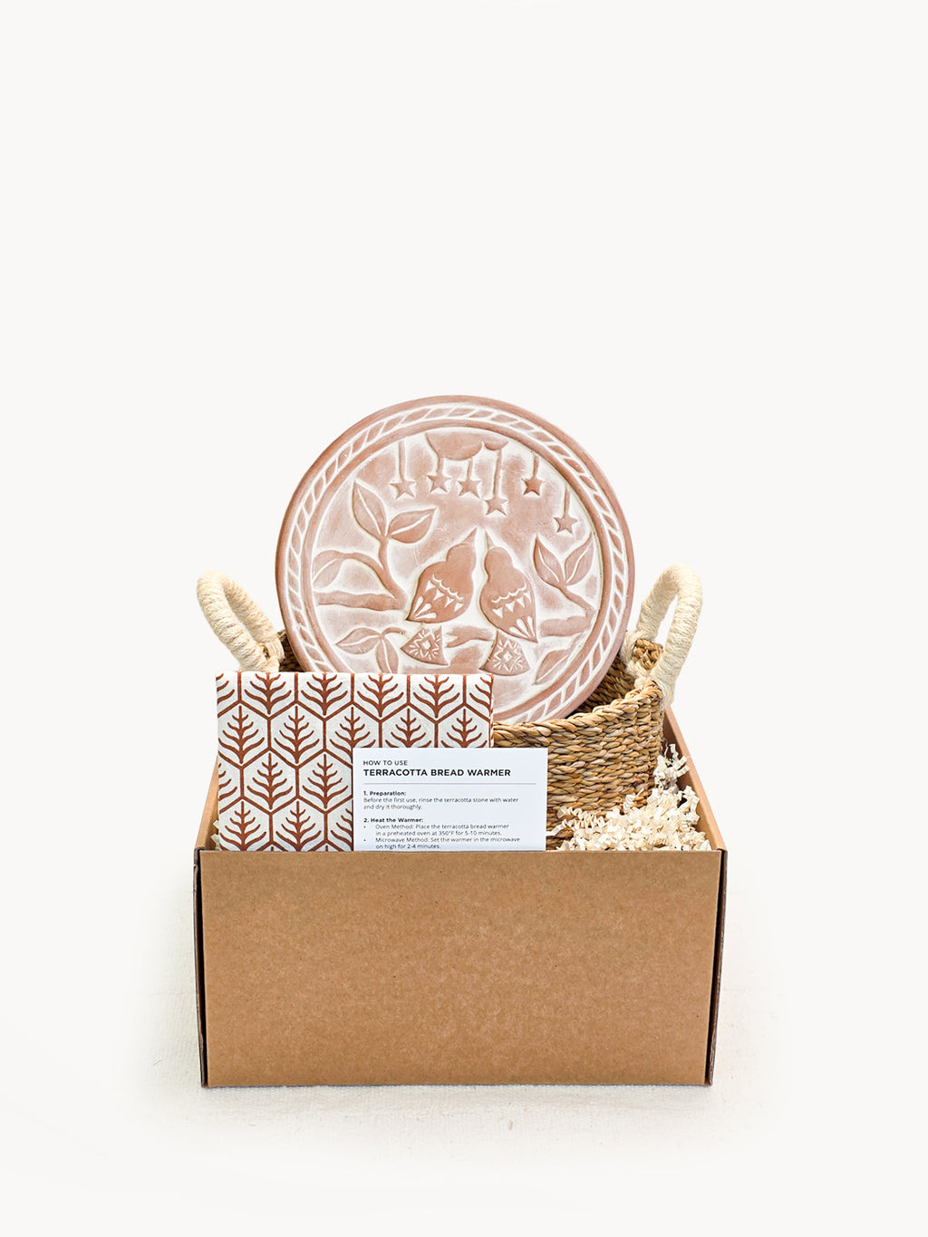 Round terracotta bread warmer with lovebird design, woven seagrass basket, and natural cotton tea towel