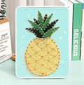 Completed yellow and green pineapple string art on a wooden board with display stand
