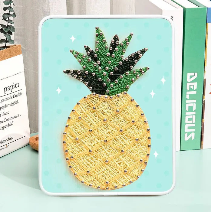 Completed yellow and green pineapple string art on a wooden board with display stand