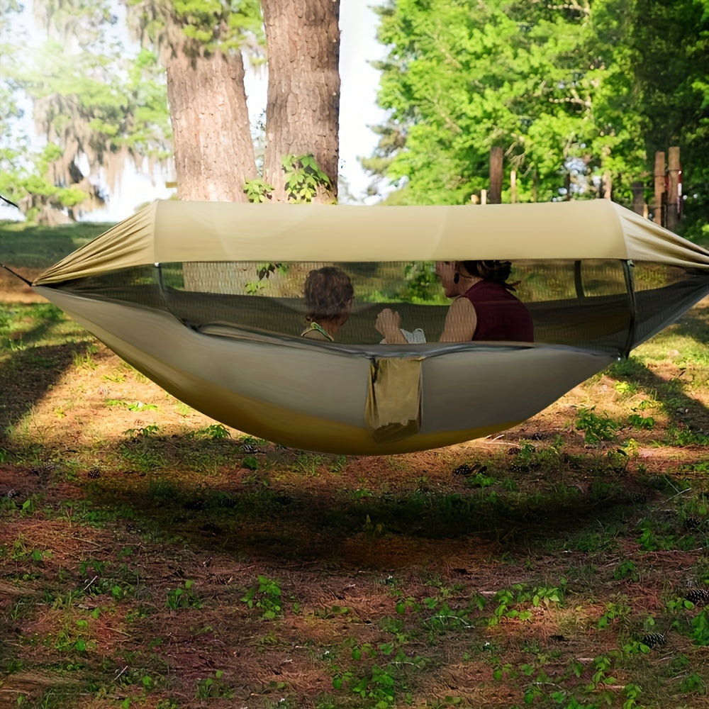 Green nylon double camping hammock with mosquito net hanging between two trees in a forest — view 2