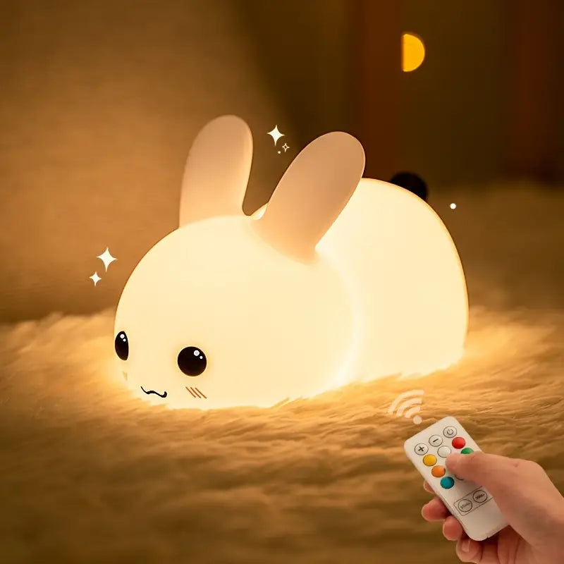 White squishy silicone bunny night light glowing with soft colors beside a remote control — view 3