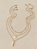 Boho multi-layer charm necklace with bar, disc, and round bead pendants on adjustable metallic chain.