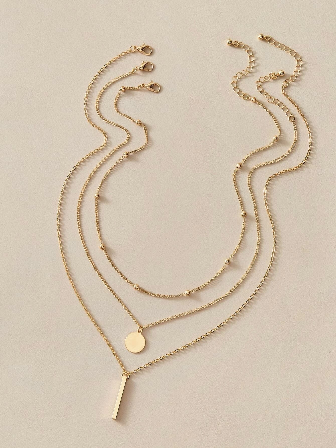 Boho multi-layer charm necklace with bar, disc, and round bead pendants on adjustable metallic chain.