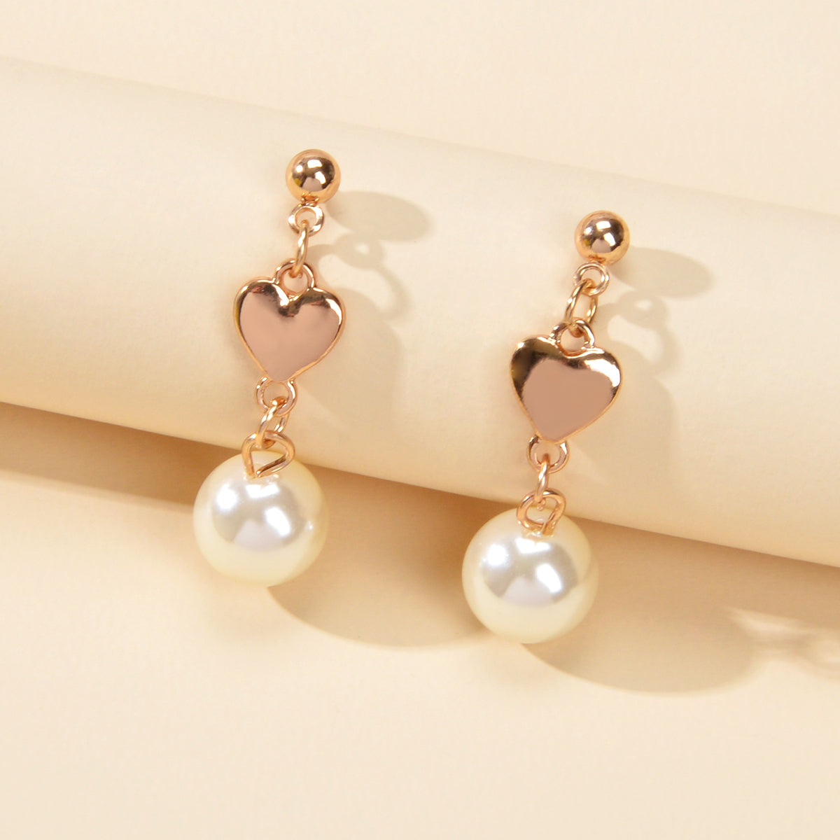 Gold heart drop earrings with simulated pearls for weddings and anniversaries on a white background