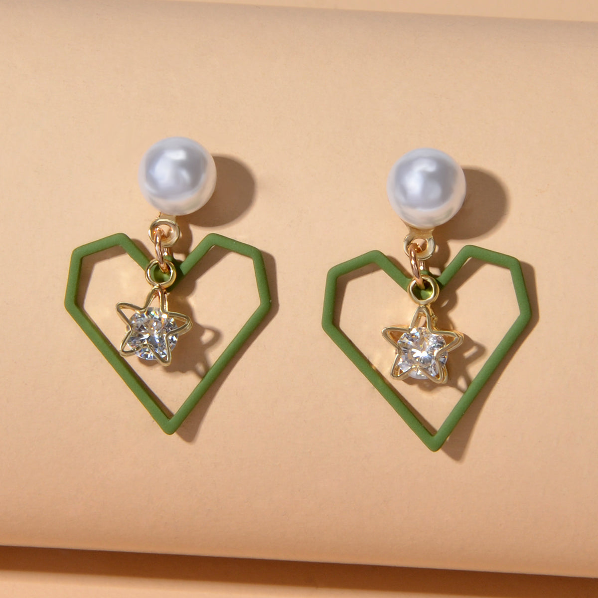 Gold tone dangle earrings featuring rhinestone star and pearl heart decorations on a white background