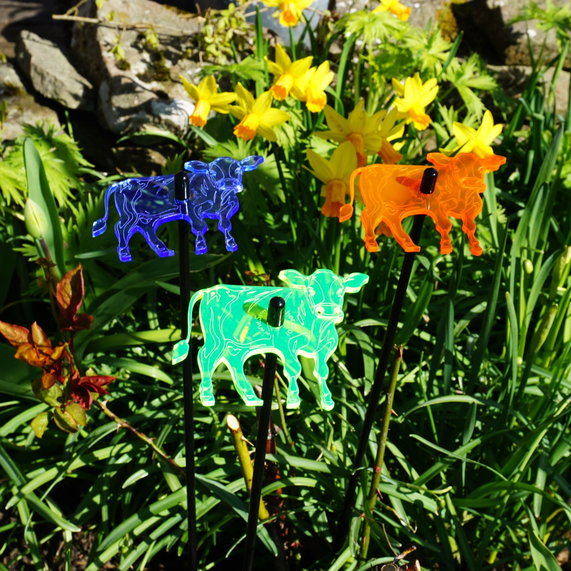 Three glowing cow garden stakes, vibrant suncatcher yard ornaments displayed in a flower bed — view 2
