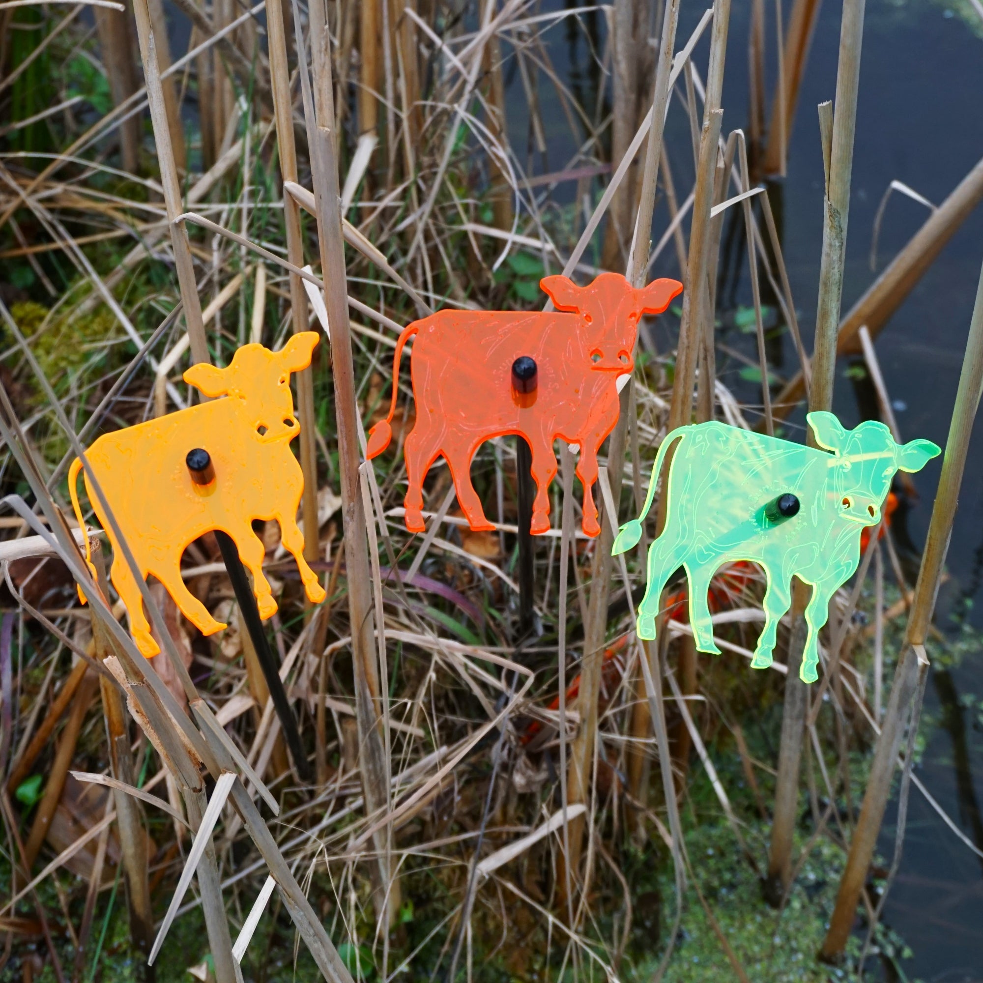 Three glowing cow garden stakes, vibrant suncatcher yard ornaments displayed in a flower bed — view 3