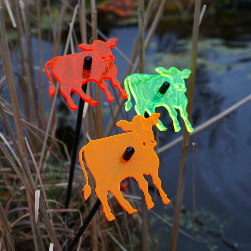 Three glowing cow garden stakes, vibrant suncatcher yard ornaments displayed in a flower bed