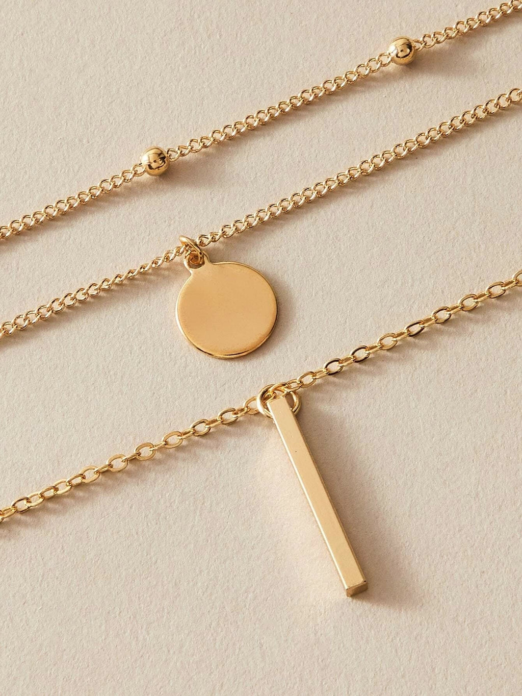 Boho multi-layer charm necklace with bar, disc, and round bead pendants on adjustable metallic chain. — view 3