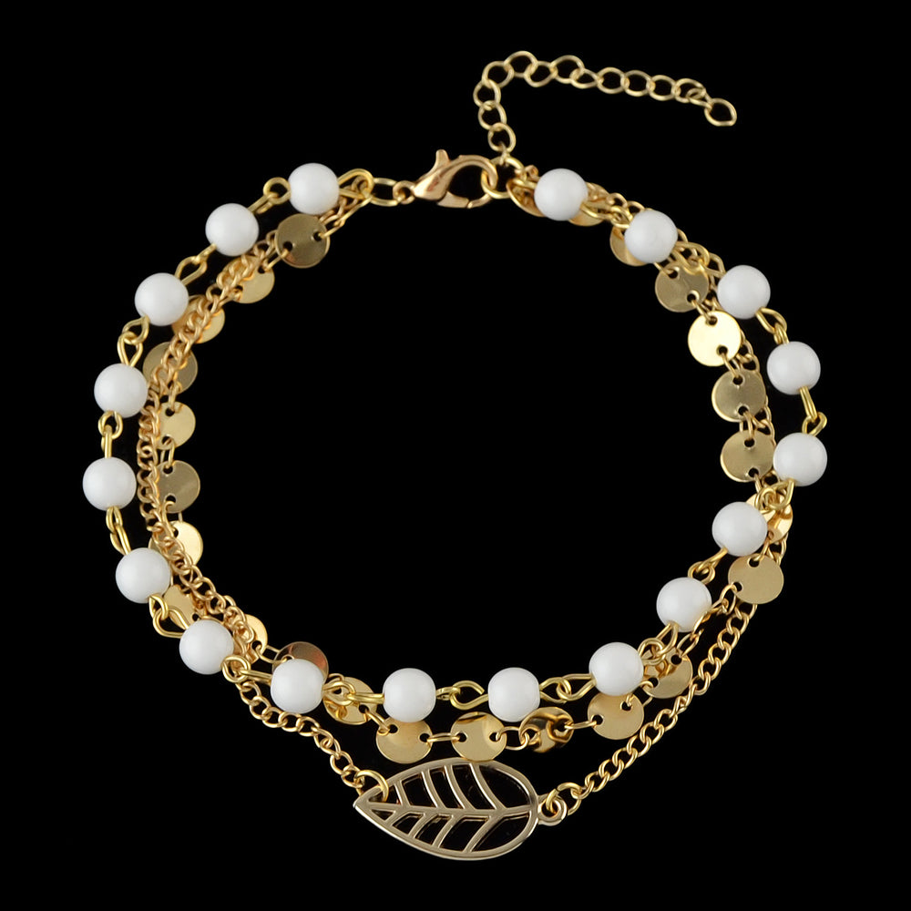 Multi-layer gold and silver tone chain anklet with white beads and leaf pendant on foot — view 2