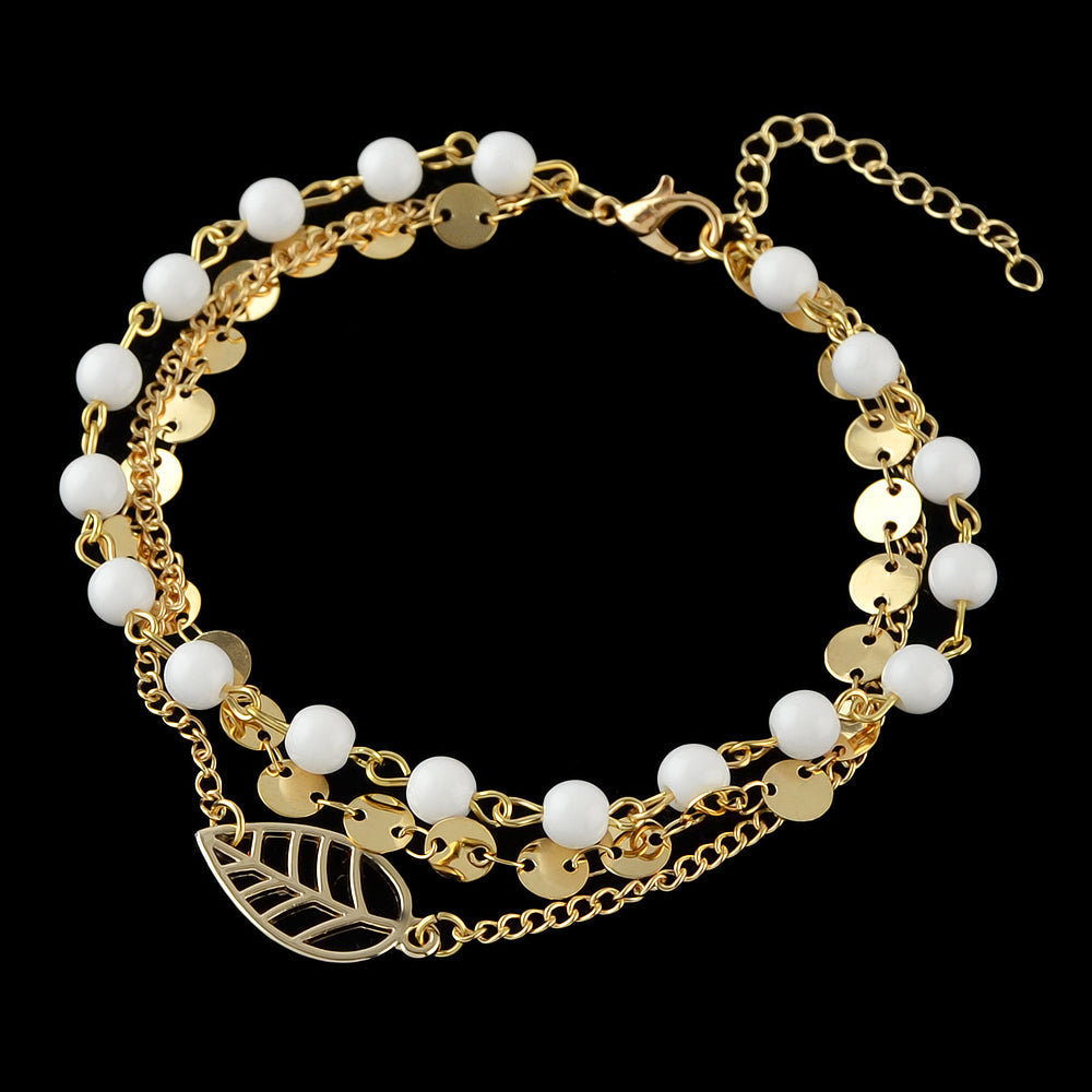 Multi-layer gold and silver tone chain anklet with white beads and leaf pendant on foot — view 3