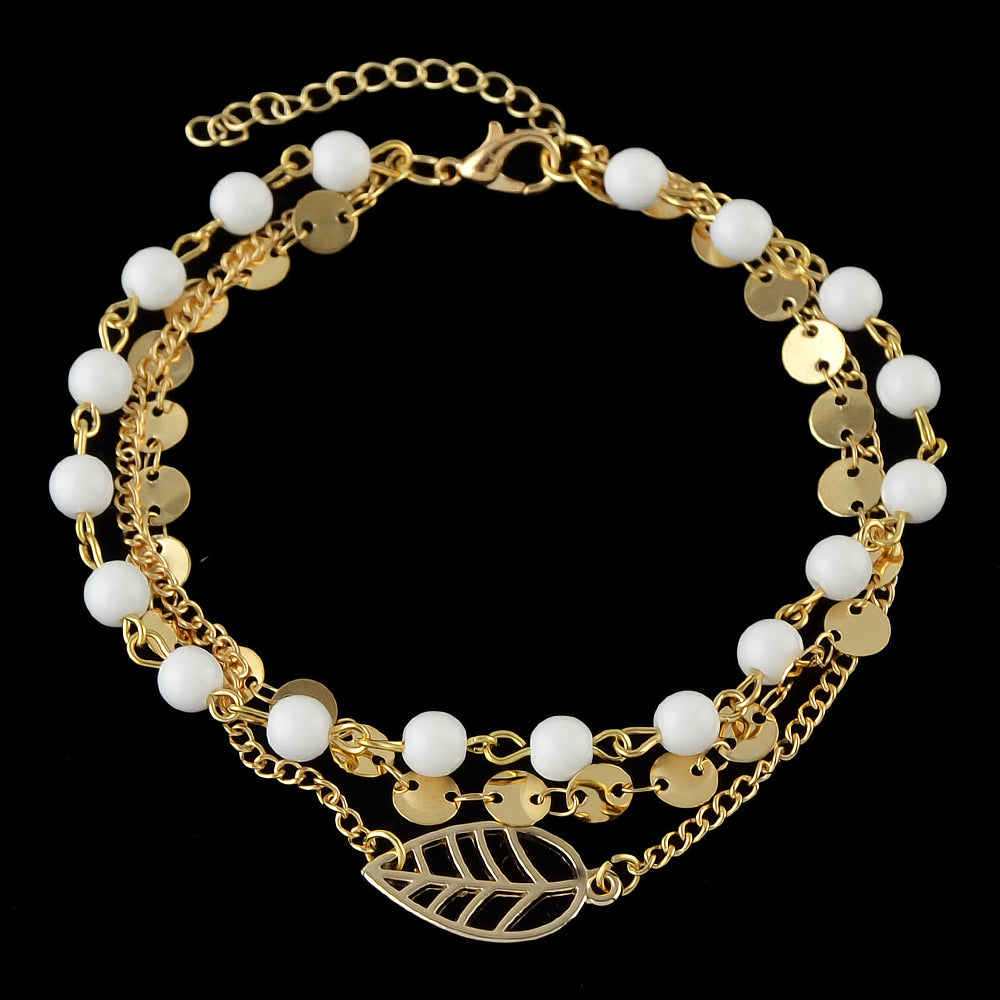 Multi-layer gold and silver tone chain anklet with white beads and leaf pendant on foot — view 4
