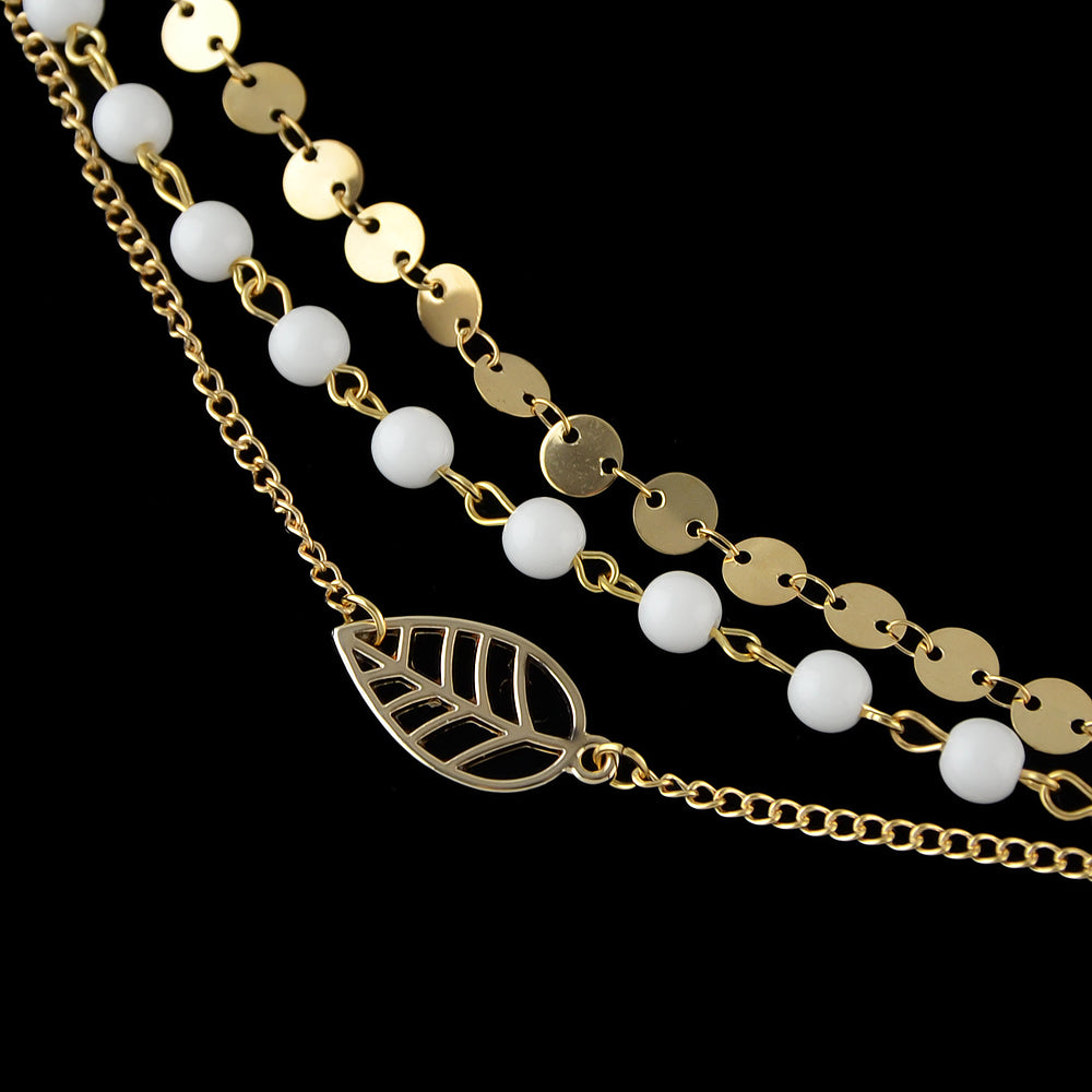 Multi-layer gold and silver tone chain anklet with white beads and leaf pendant on foot — view 5