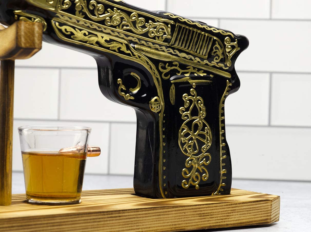 Black and gold hand-painted pistol whiskey decanter with two shot glasses on wooden display stand — view 3