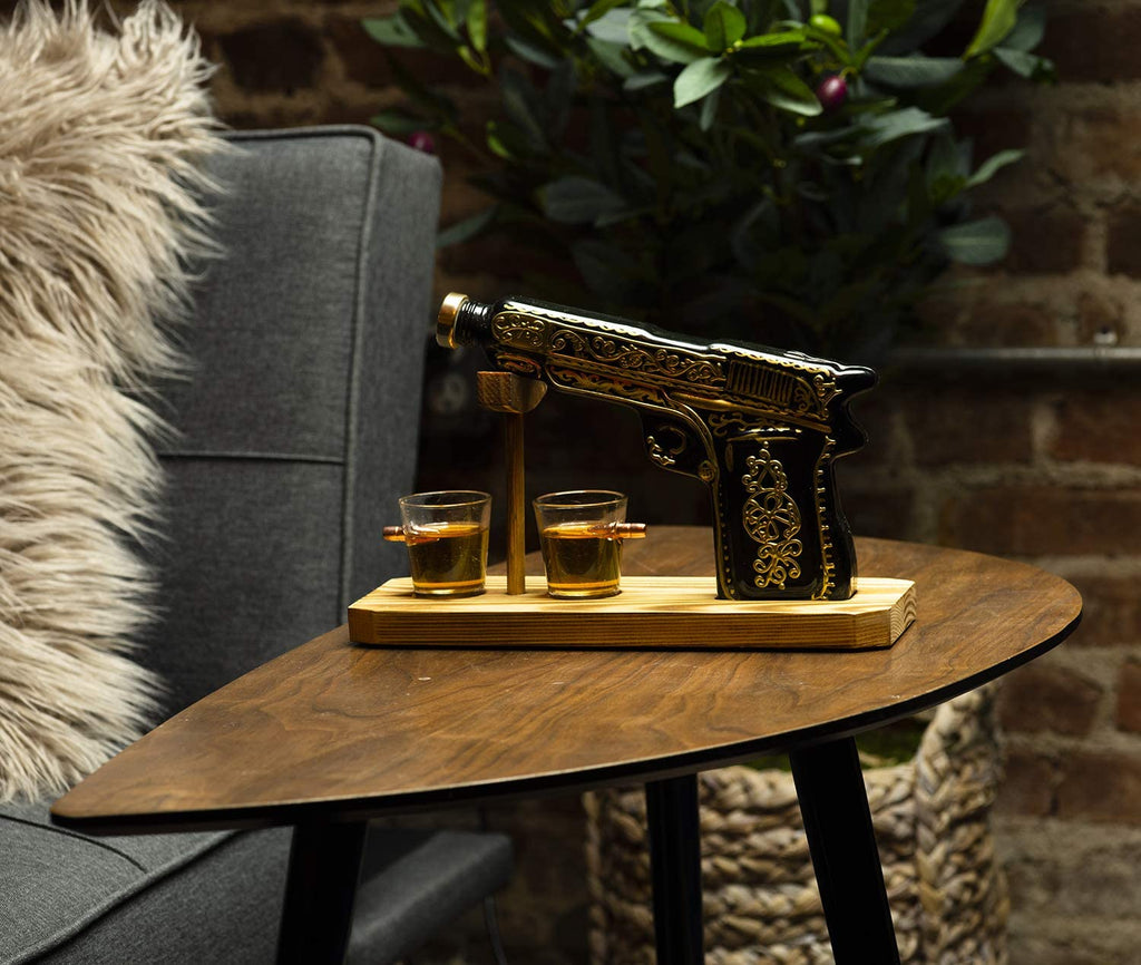 Black and gold hand-painted pistol whiskey decanter with two shot glasses on wooden display stand — view 2