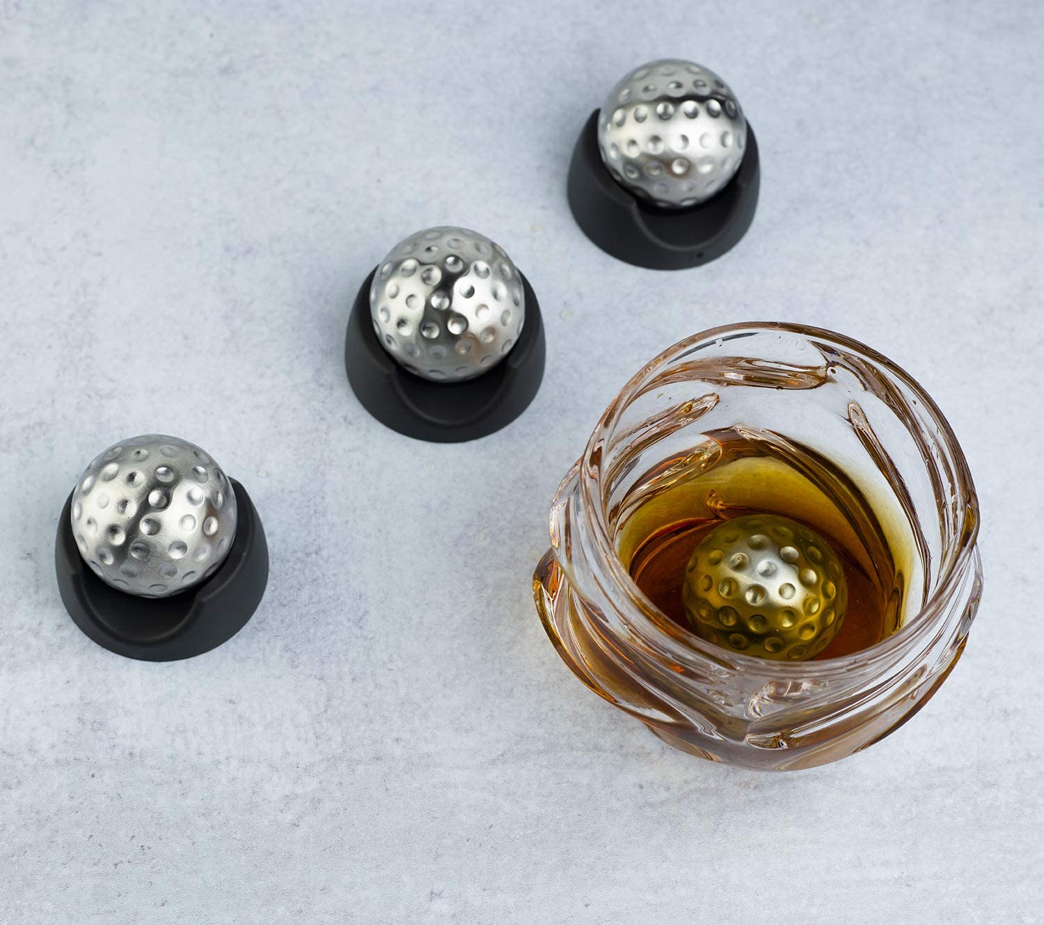 Stainless steel golf ball shaped whiskey stones chilling in a crystal glass of bourbon — view 5
