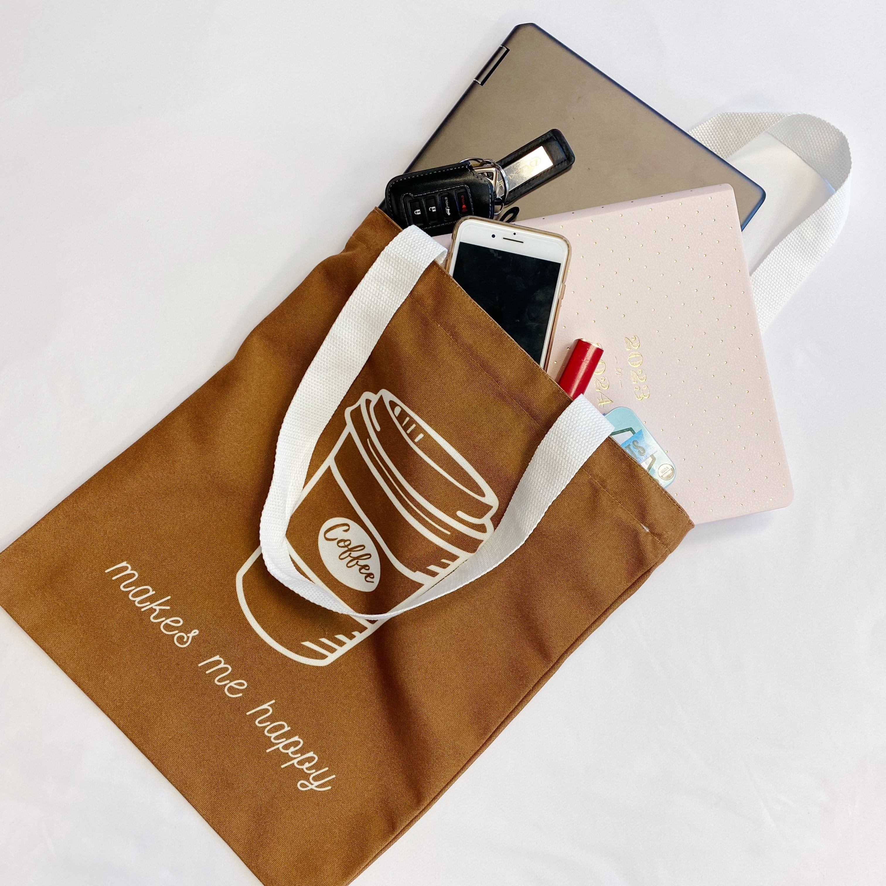 White canvas tote bag with graphic print and shoulder strap carrying books and a laptop — view 3