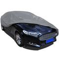Medium grey nonwoven car cover securely fitted over a sedan for outdoor weather protection