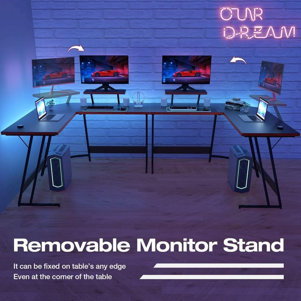 Black L-shaped gaming desk with carbon fiber finish, red accents, monitor riser, and metal Z-shaped legs — view 4