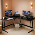Black L-shaped gaming desk with carbon fiber finish, red accents, monitor riser, and metal Z-shaped legs