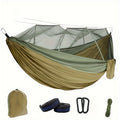 Green nylon double camping hammock with mosquito net hanging between two trees in a forest