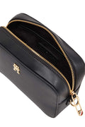Women's black faux-leather crossbody shoulder bag with adjustable logo strap and front monogram plaque