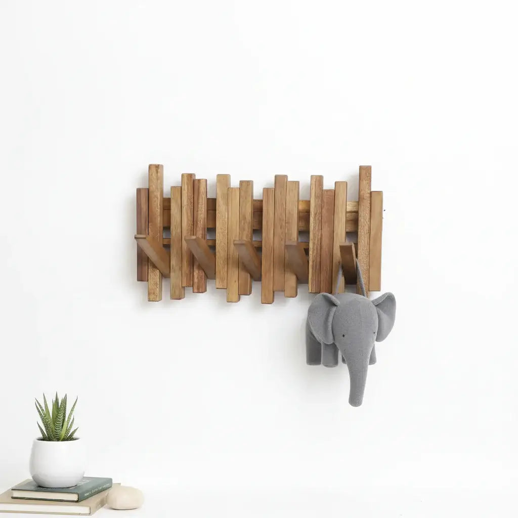 Acacia wood wall mounted coat rack with flip down hooks hanging in a modern entryway