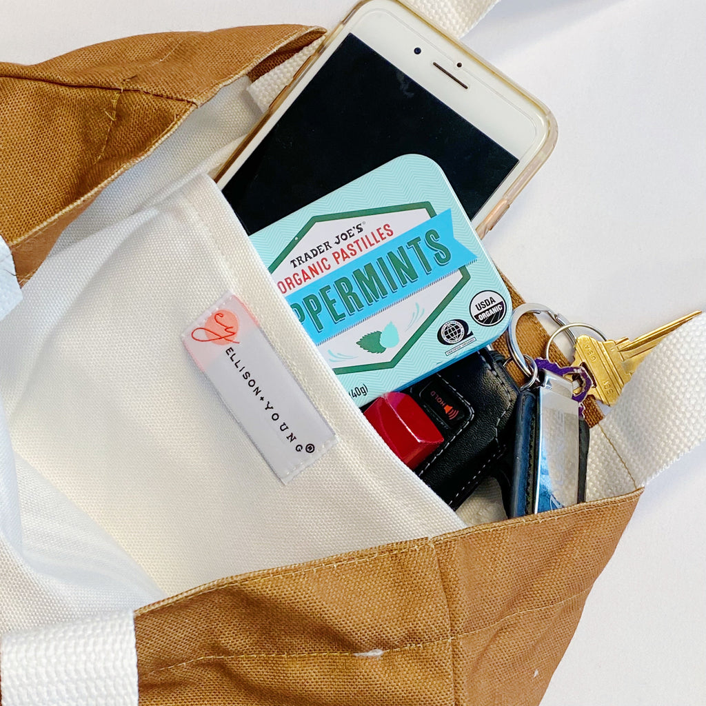 White canvas tote bag with graphic print and shoulder strap carrying books and a laptop — view 4