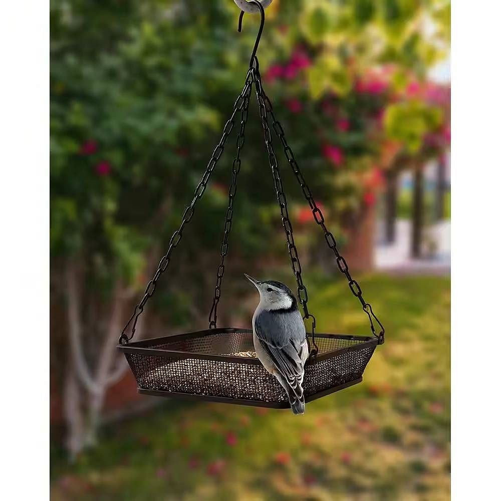 Black iron mesh bird feeder and seed tray hanging from a chain in an outdoor garden — view 2