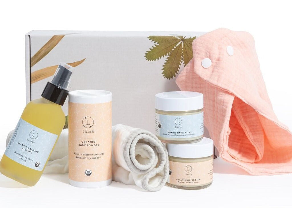Organic baby skincare gift set in beautiful box featuring balms, oils, powder, and soft bibs