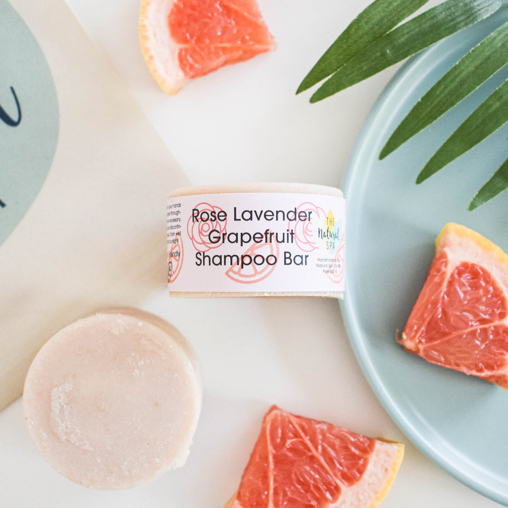 Solid rose lavender and grapefruit shampoo bar beside natural ingredients and plastic free packaging
