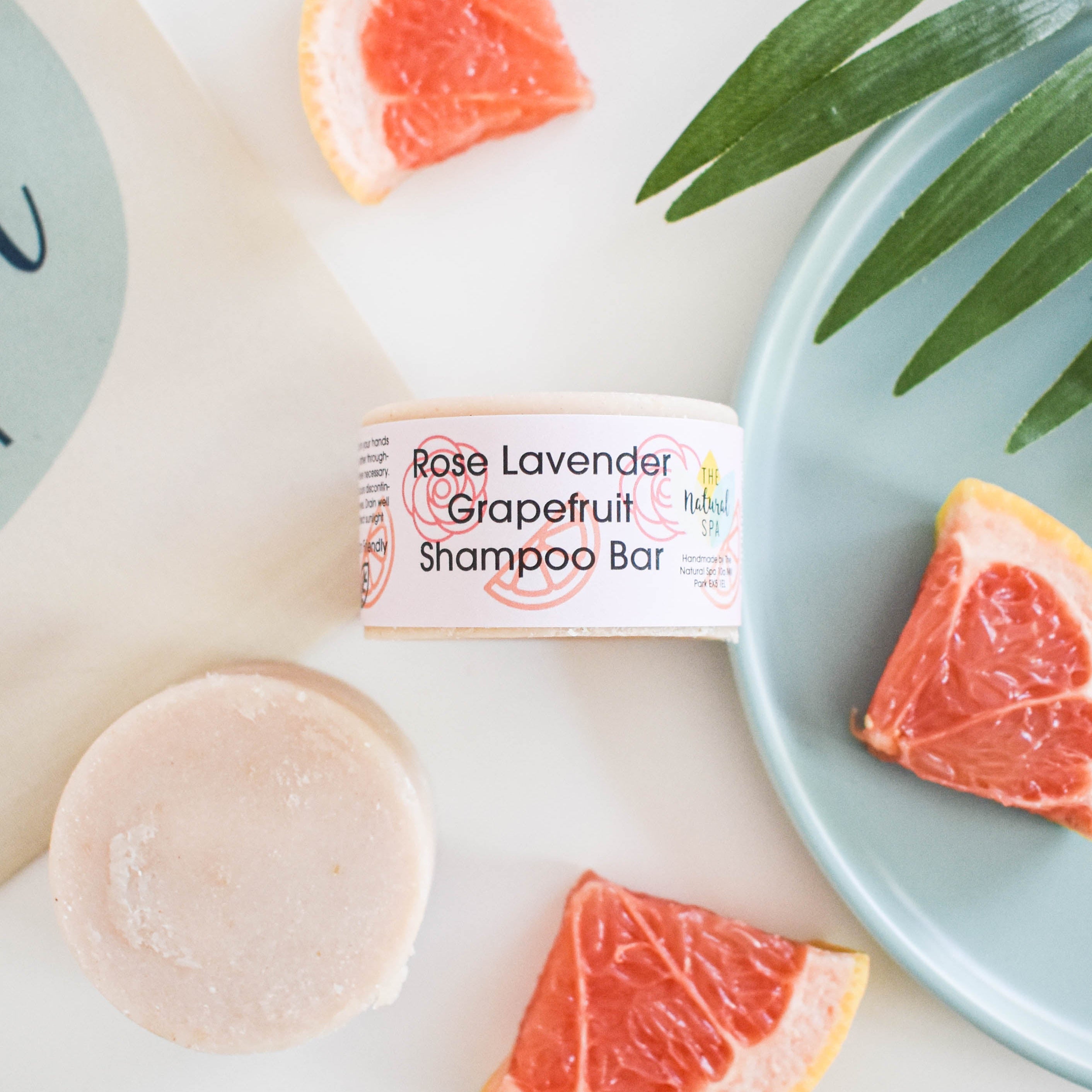 Solid rose lavender and grapefruit shampoo bar beside natural ingredients and plastic free packaging