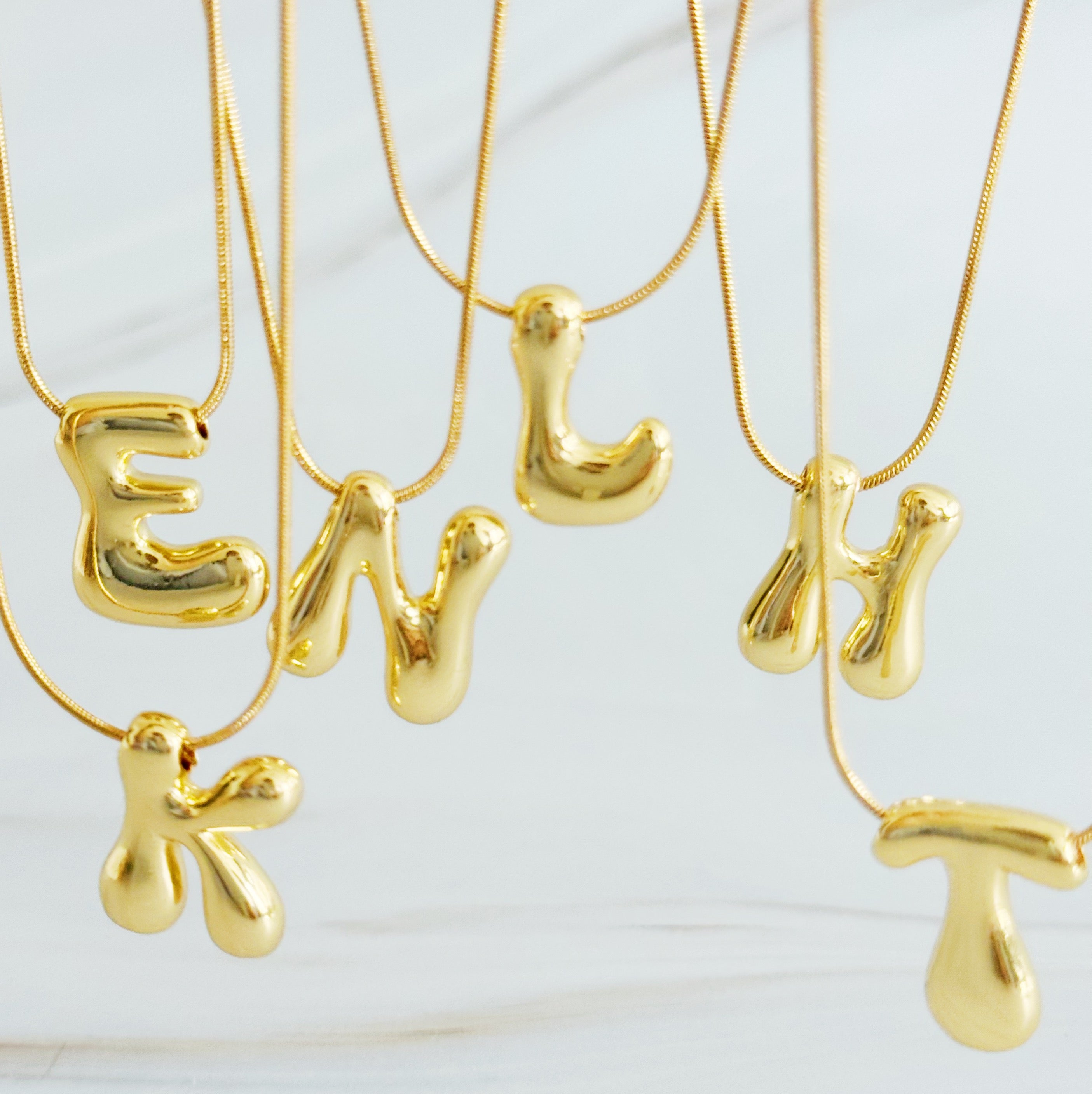Gold plated balloon letter initial necklace with a stainless steel chain on a plain background