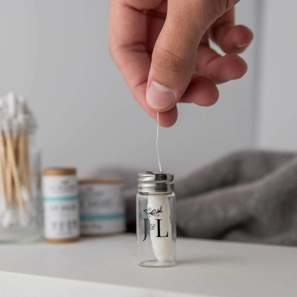 Biodegradable mint dental floss roll in a reusable clear glass dispenser bottle for sustainable oral care
