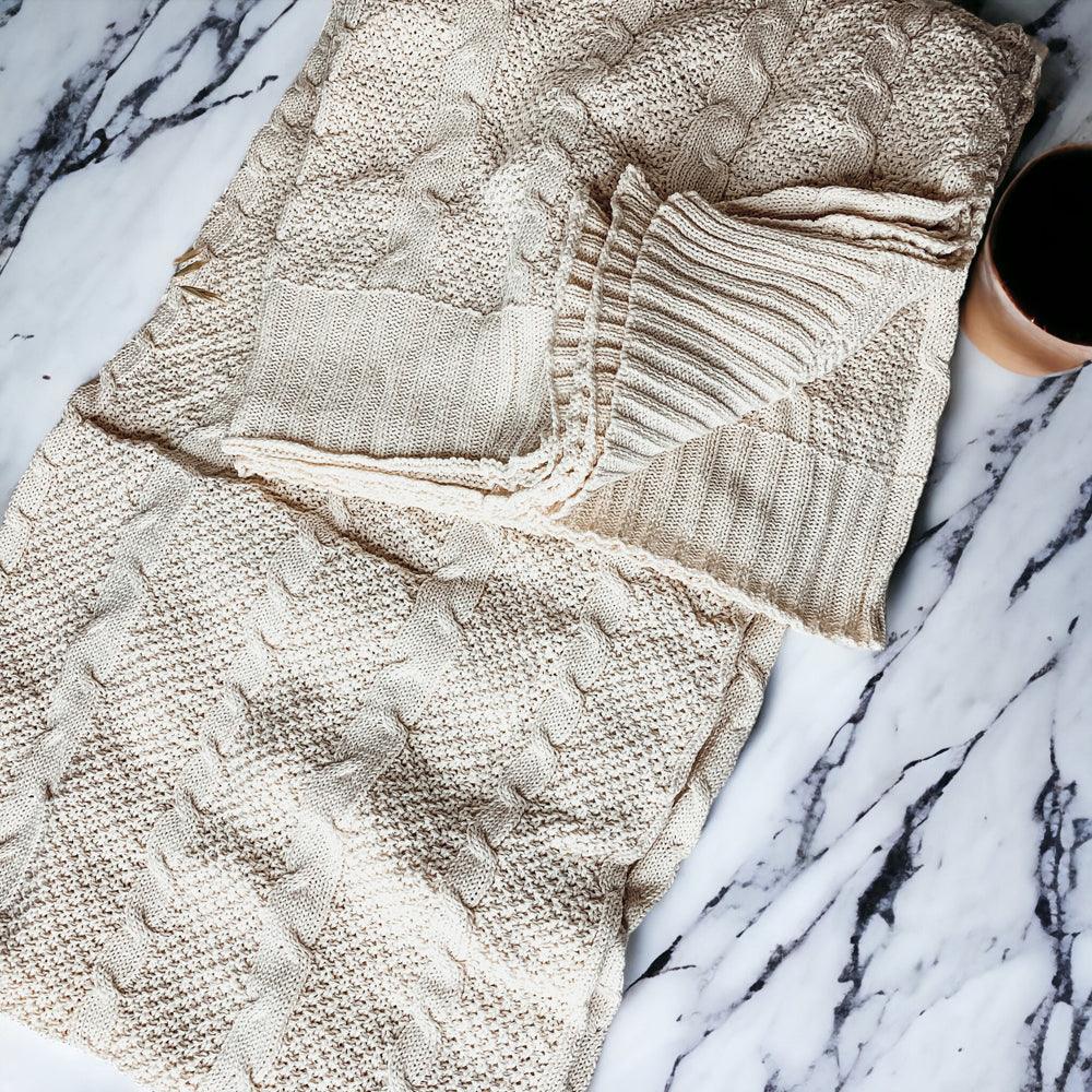 Ivory cable knit sweater throw blanket made of a soft cotton blend, draped elegantly. — view 4