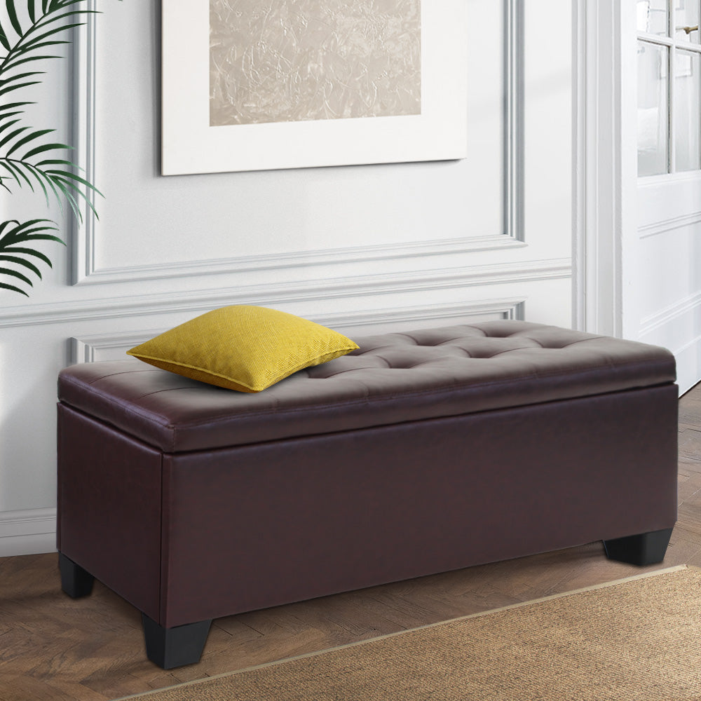 Brown faux leather storage ottoman blanket box with wooden legs and lift-up cushioned lid.
