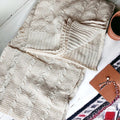 Ivory cable knit sweater throw blanket made of a soft cotton blend, draped elegantly.