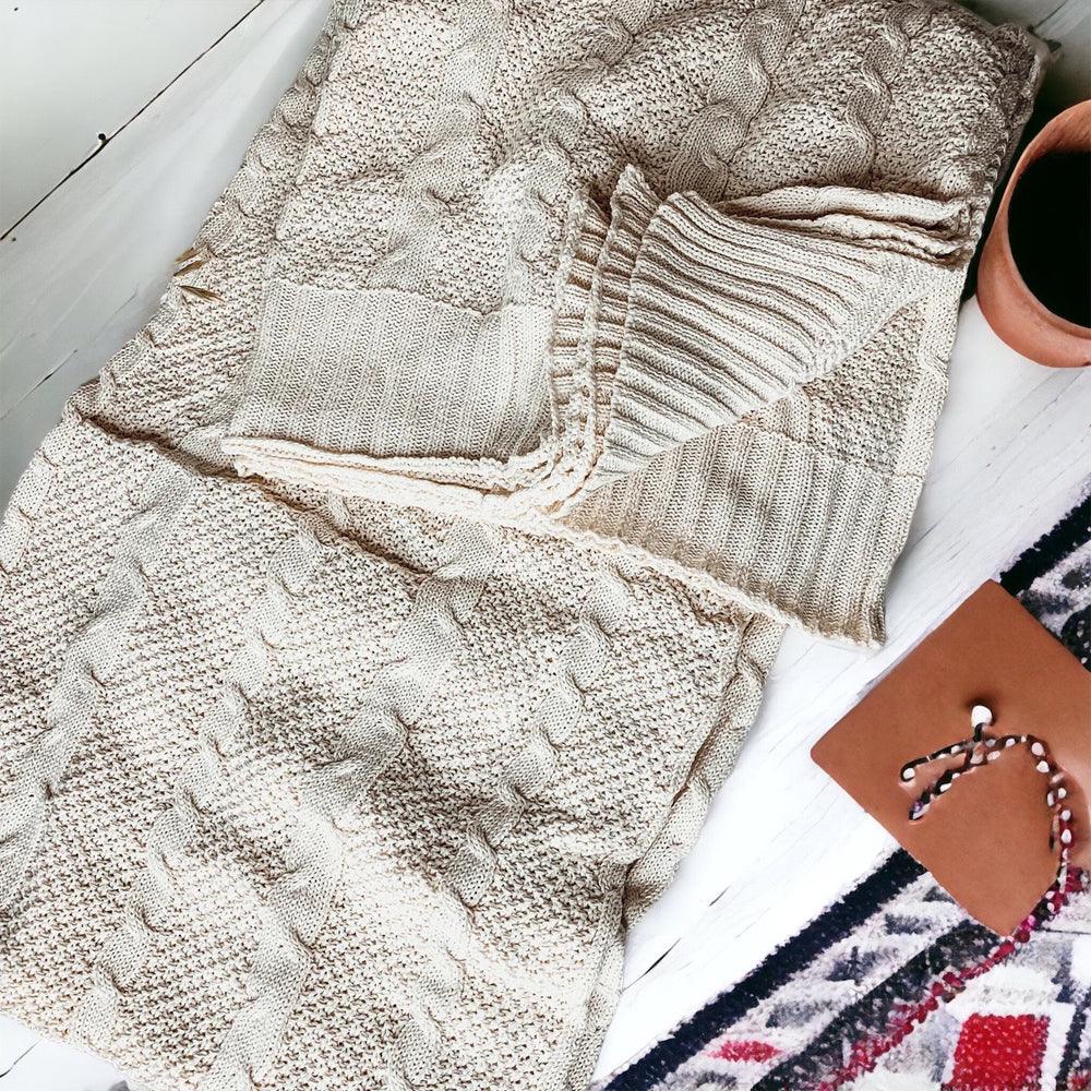 Ivory cable knit sweater throw blanket made of a soft cotton blend, draped elegantly.