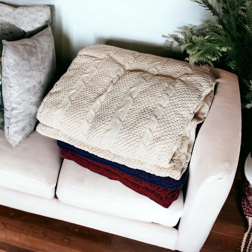 Ivory cable knit sweater throw blanket made of a soft cotton blend, draped elegantly. — view 3