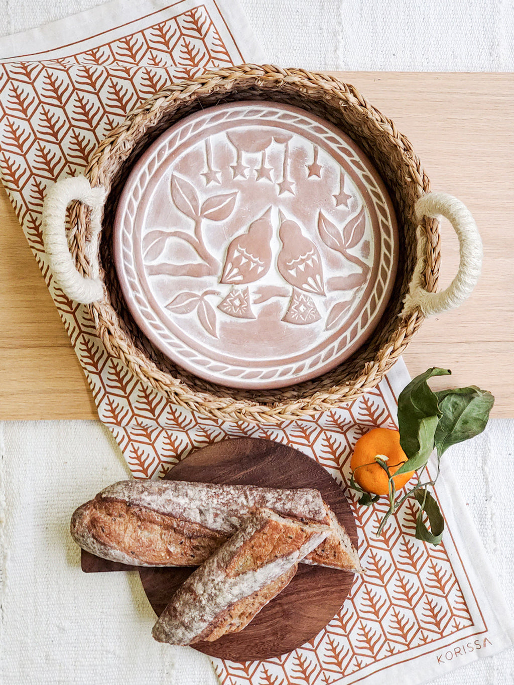 Round terracotta bread warmer with lovebird design, woven seagrass basket, and natural cotton tea towel — view 2