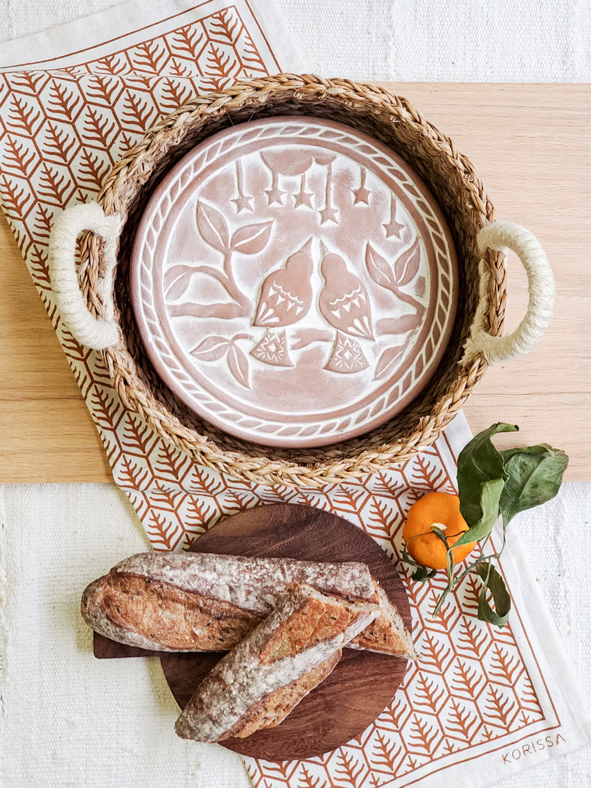Round terracotta bread warmer with lovebird design, woven seagrass basket, and natural cotton tea towel — view 2