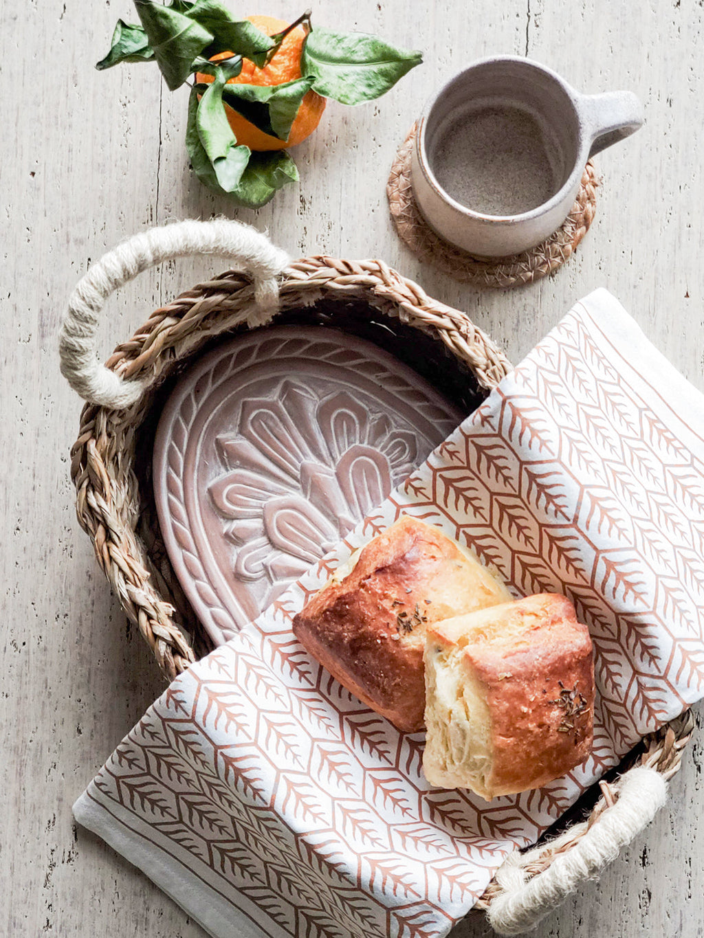 Terracotta bread warmer with engraved flower, woven seagrass serving basket, and natural cotton tea towel. — view 5