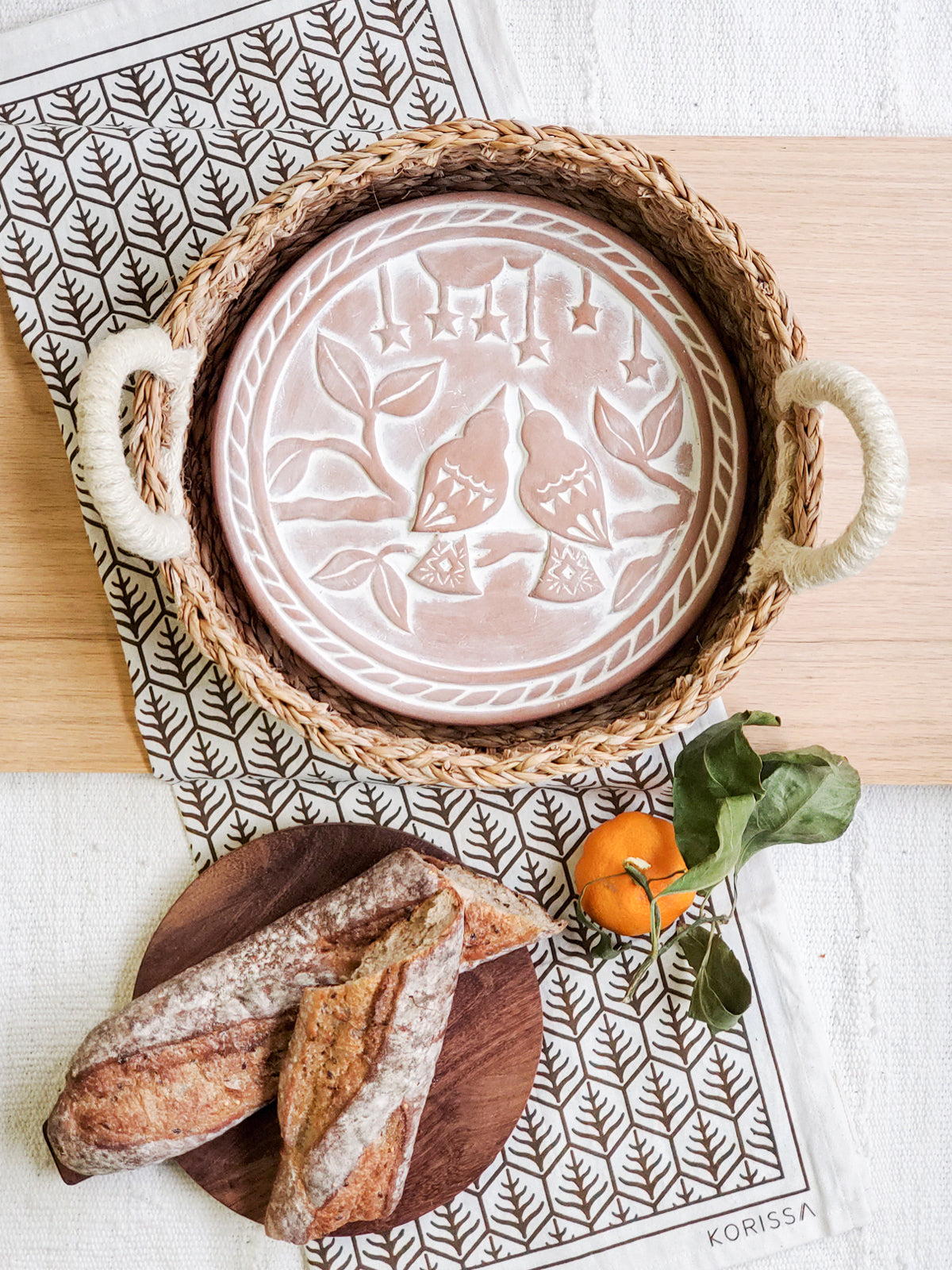 Round terracotta bread warmer with lovebird design, woven seagrass basket, and natural cotton tea towel — view 3