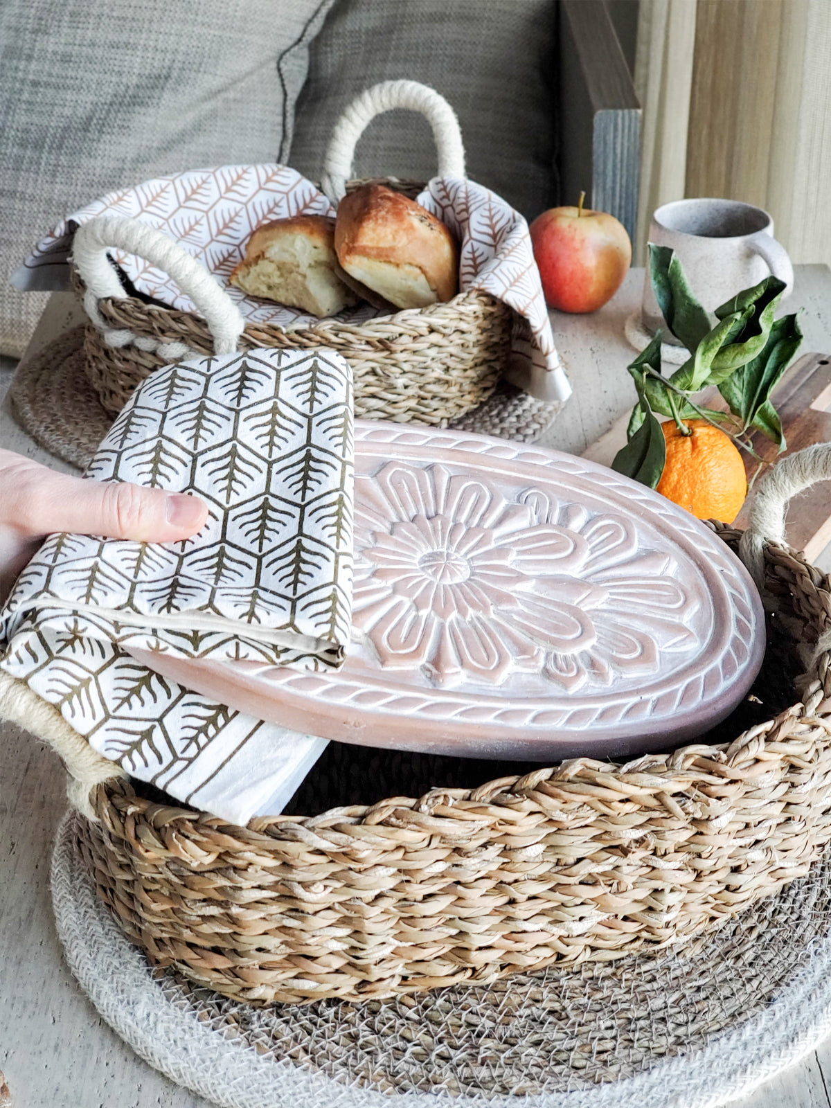 Terracotta bread warmer with engraved flower, woven seagrass serving basket, and natural cotton tea towel. — view 2