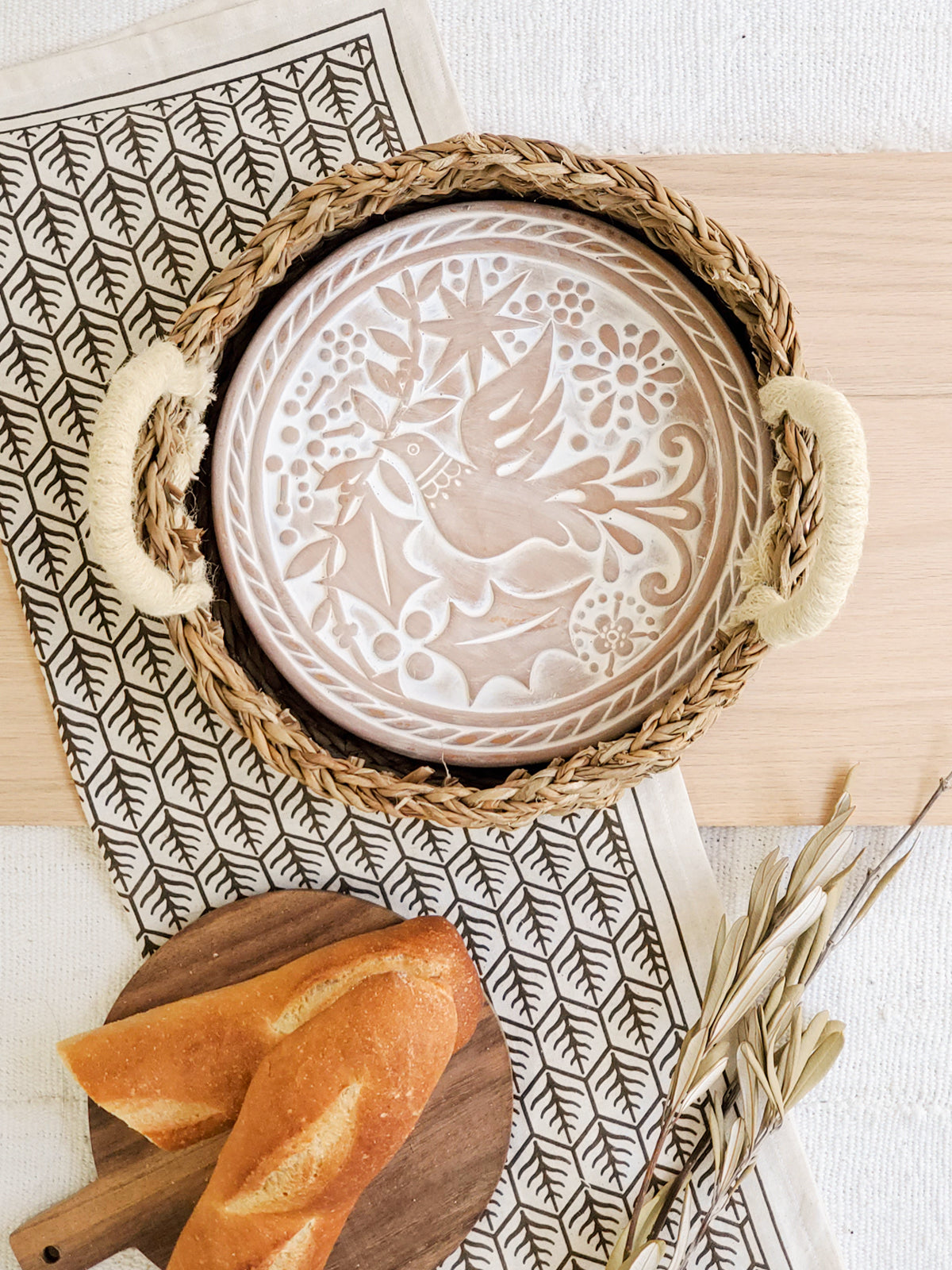 Round terracotta bread warmer with bird engraving inside a natural seagrass basket and cotton tea towel — view 2