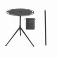Portable round camping table with telescopic light pole and tripod base on outdoor terrain